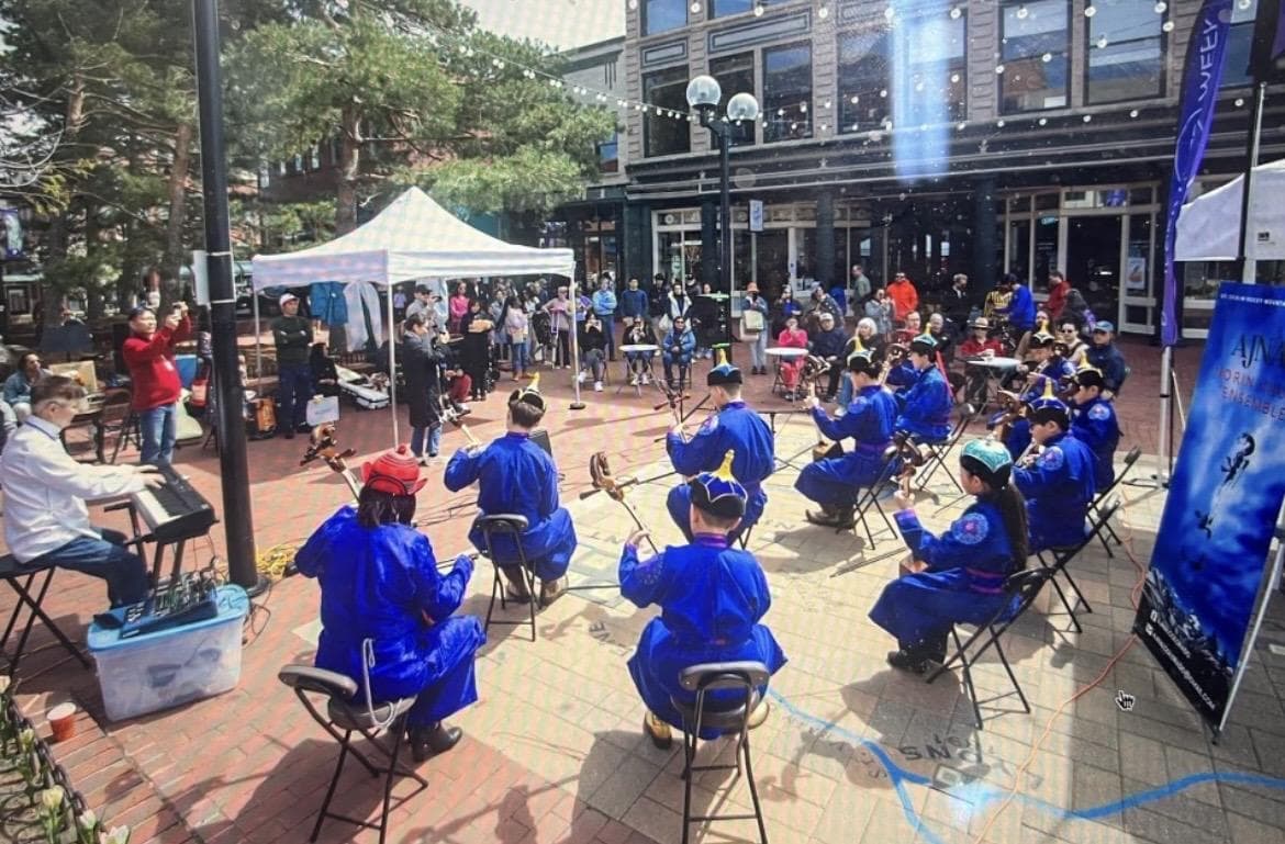 Ajnai Ensemble seated in blue deels, playing morin khuur for a crowd during a Boulder performance.