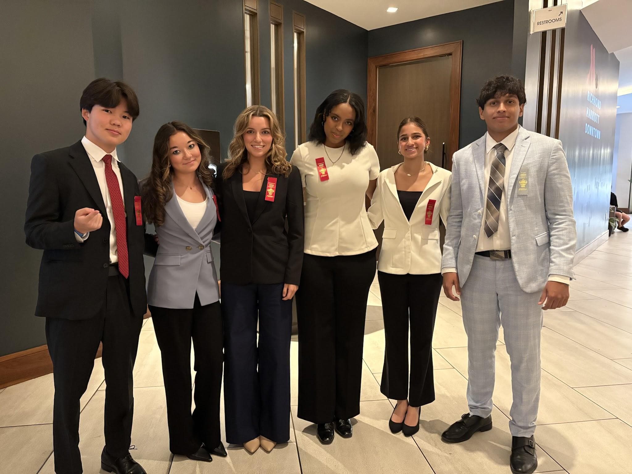 Eric at the far left in a black suit and red ribbon, with other competitors in a hotel hallway at the national tournament.