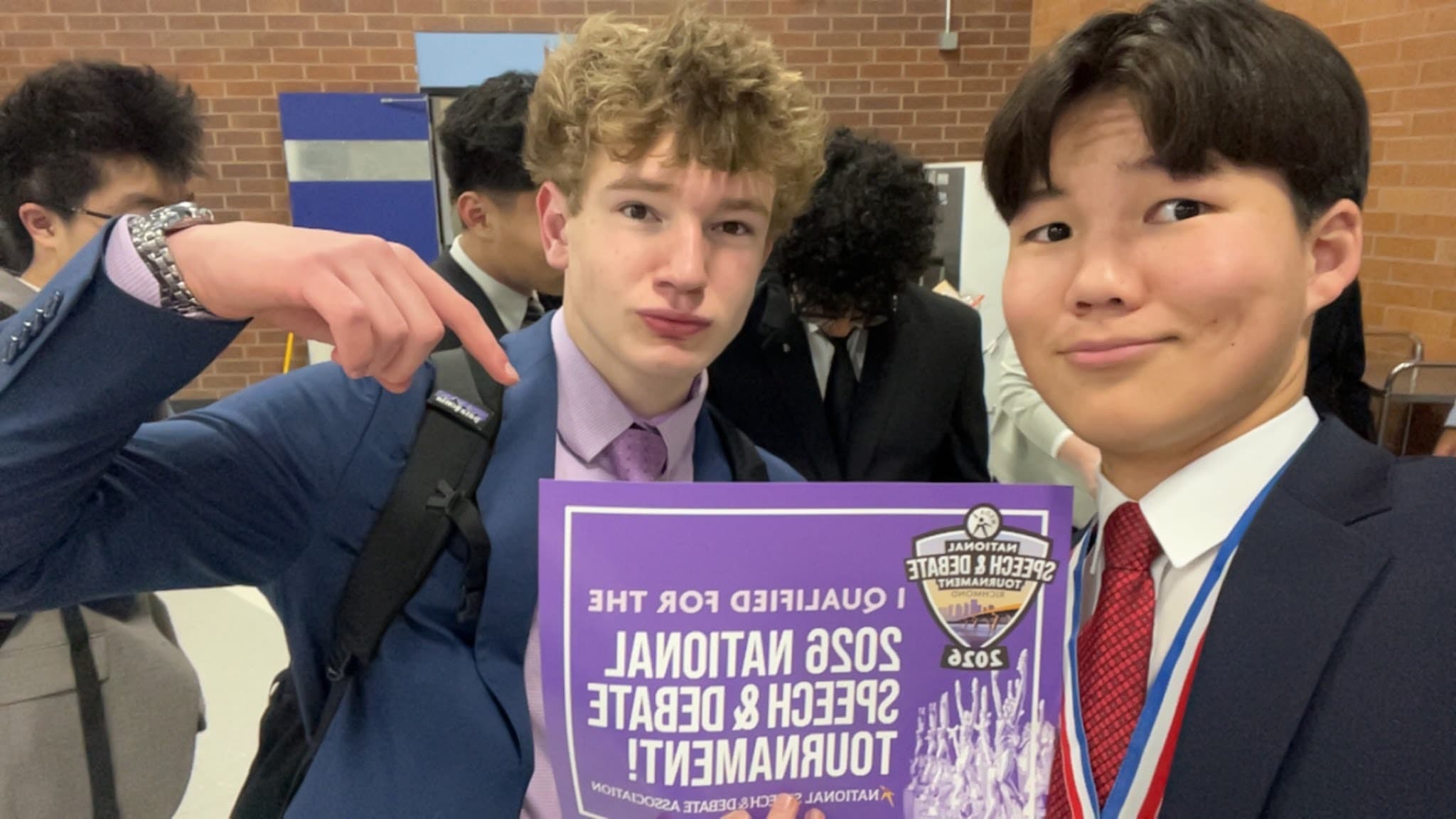 Eric in the foreground, in a navy suit and red tie, with teammates and an upside-down national qualifier sign.