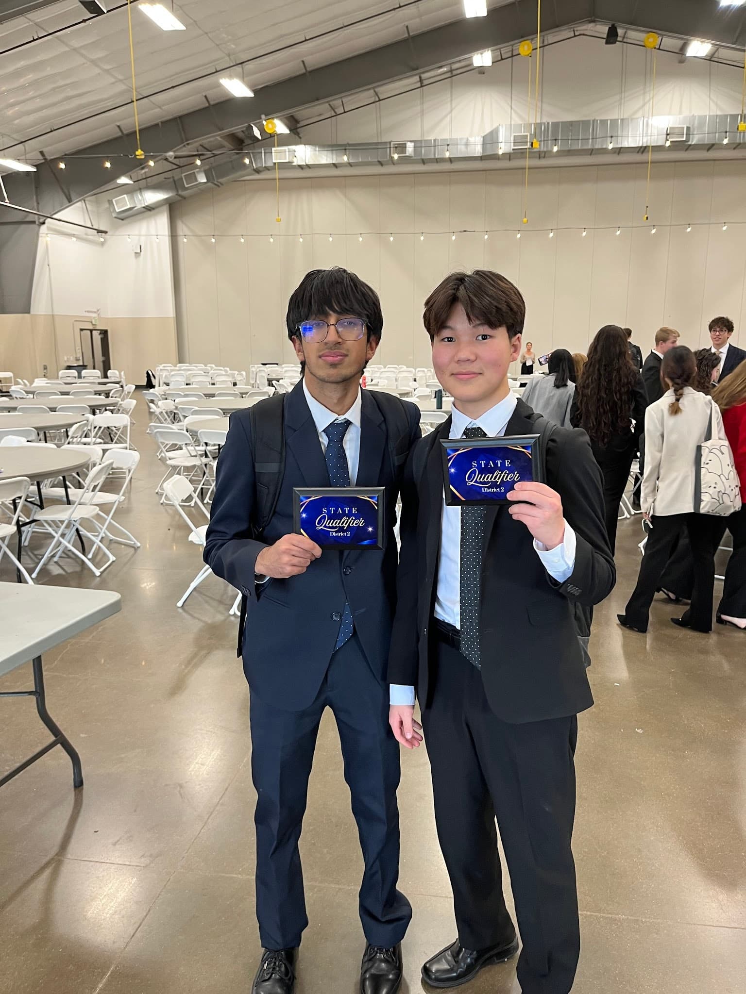 Eric, on the right, and a teammate holding District 2 state-qualifier plaques in a conference hall.
